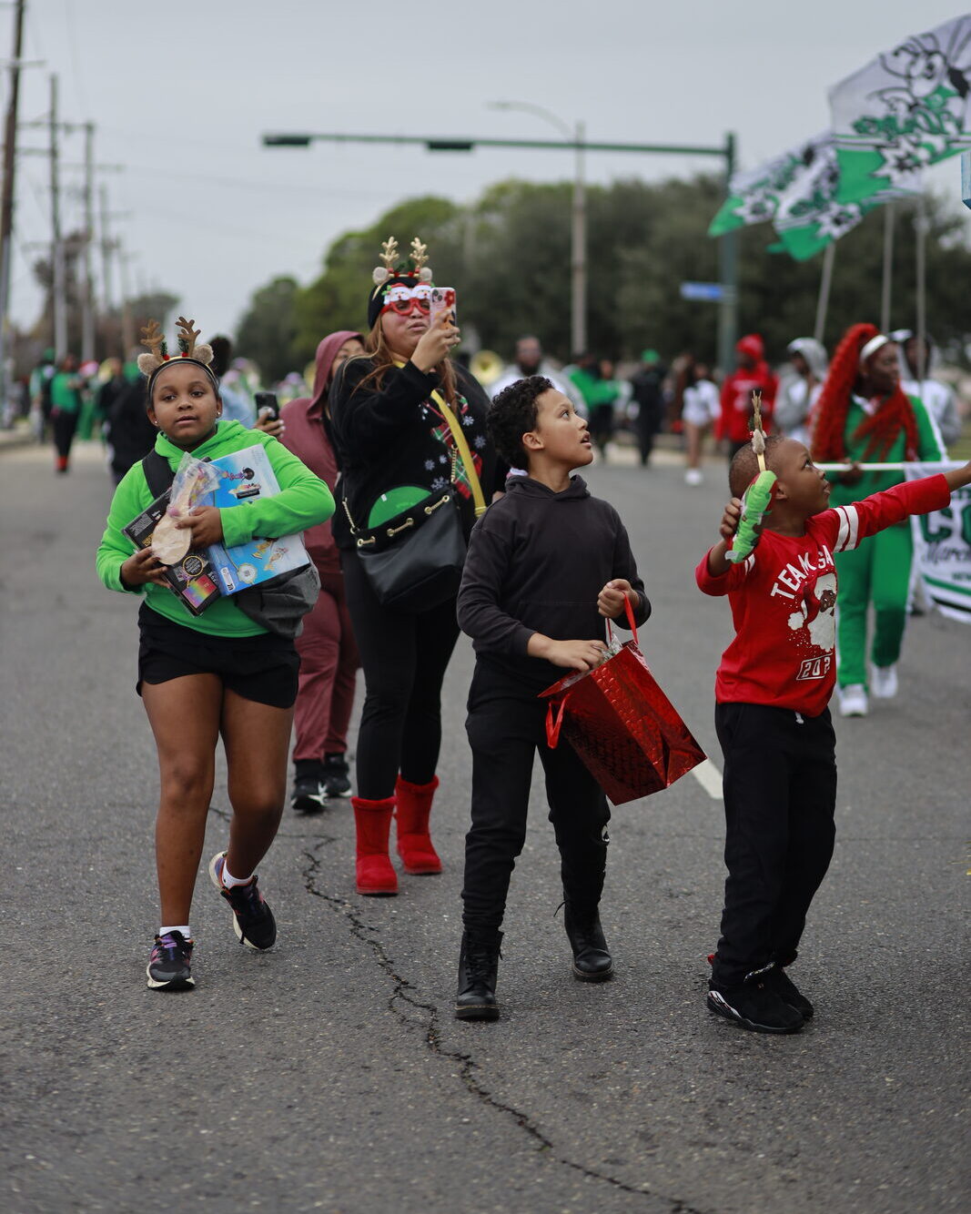 Children in holiday accessories carrying gifts along the parade route